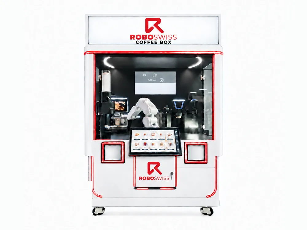 The CoffeeBOX machine: a robotic arm behind the glass, an ordering touchscreen and two serving hatches.